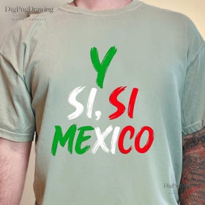 Può includere: Una t-shirt a maniche corte color verde salvia con il testo Y SI, SI MEXICO stampato in stile pennellata. Le lettere sono colorate in verde, bianco e rosso, riflettendo i colori della bandiera messicana, disposte su tre righe distinte.