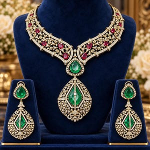 May include: A gold necklace and matching drop earrings set featuring intricate filigree metalwork, encrusted with numerous small white diamonds, vibrant red rubies, and large, pear-shaped green emerald gemstones in a detailed, ornate arrangement.