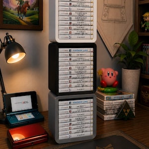 Peut inclure: Une pile verticale de trois cubes de rangement carrés blancs, noirs et gris, contenant chacun une rangée de boîtiers de jeux Nintendo 3DS. Les titres incluent Pokémon Luna, Luigi's Mansion 2 et diverses éditions de Yo-Kai Watch, soigneusement organisés dans les étagères ouvertes.