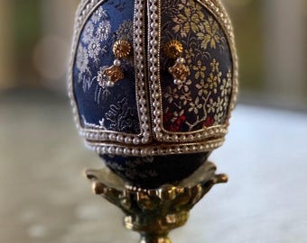 Decorated goose egg Art. Egg covered with blue brocade fabric. Opens to reveal an Asian women in a kimono. Doors trim men with small pearls