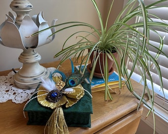 Emerald green  fabric covered box decorated with vintage jewelry and peacock feathers. Beautiful gold ribbon background and a gold tassel