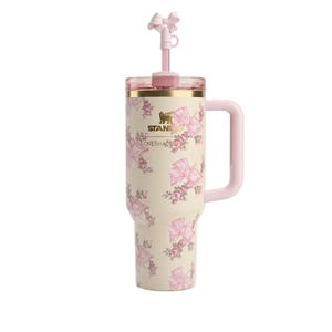 Puede incluir: Un vaso t&eacute;rmico de color crema con asa, que presenta un estampado de flores y lazos rosas. Los logotipos de Stanley y LoveShackFancy est&aacute;n impresos en el frente. Incluye una tapa transparente y una pajita rosa con un lazo decorativo.
