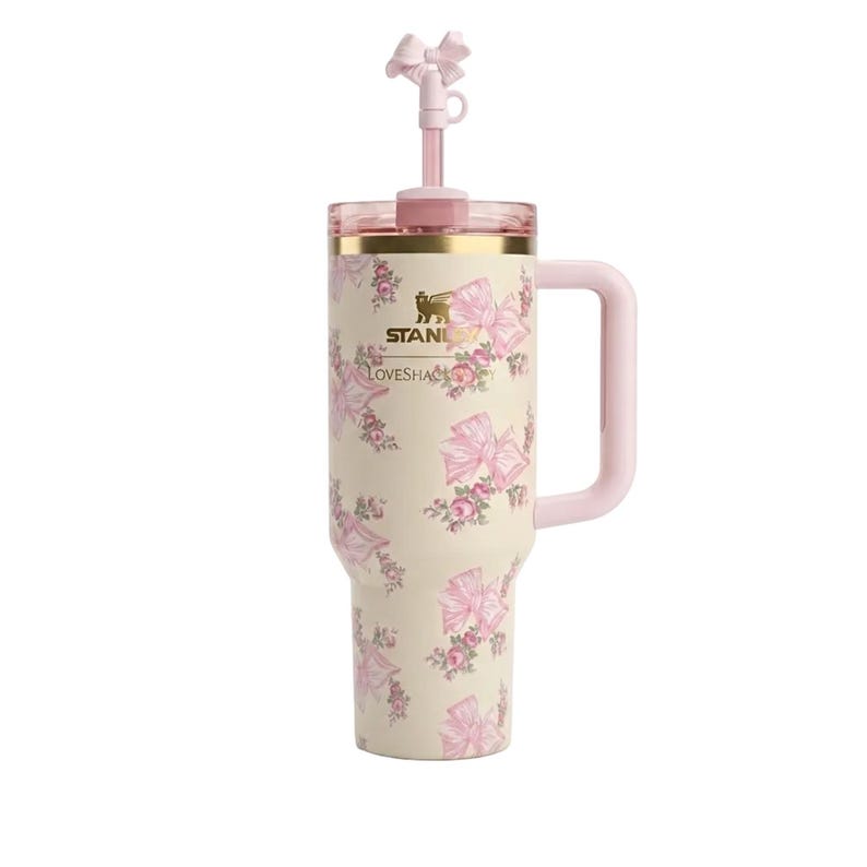 Puede incluir: Un vaso t&eacute;rmico de color crema con asa, que presenta un estampado de flores y lazos rosas. Los logotipos de Stanley y LoveShackFancy est&aacute;n impresos en el frente. Incluye una tapa transparente y una pajita rosa con un lazo decorativo.