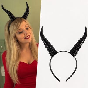 Peut inclure: Un serre-tête noir doté de deux grandes cornes de diable incurvées et striées pointant vers le haut. Les cornes présentent une finition brillante et une texture segmentée, fixées sur un bandeau noir fin et flexible pour la tête.