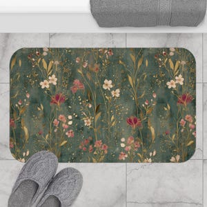 May include: A rectangular bath mat featuring a dark teal background with a botanical pattern of gold, pink, and white wildflowers. The design includes delicate stems, leaves, and scattered gold speckles across the surface of the mat.