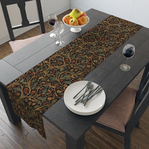 May include: A rectangular table runner featuring a dark black background with an intricate botanical pattern of swirling golden vines, muted green leaves, and small red berries, draped across a dark wooden dining table with place settings.