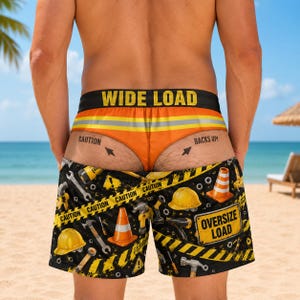May include: Orange and black swim shorts featuring a construction theme with yellow caution tape patterns, traffic cones, hard hats, and tools. The waistband reads WIDE LOAD, and the back of the shorts features the text OVERSIZE LOAD.