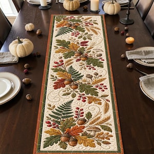 May include: A rectangular table runner featuring a quilted cream-colored fabric with an intricate embroidered pattern of autumn leaves, acorns, red berries, wheat stalks, and ferns, bordered by thin orange and dark green fabric trim.
