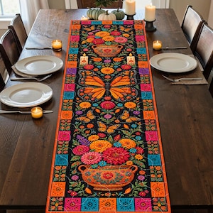 May include: A rectangular table runner featuring a black background with a vibrant pattern of orange monarch butterflies, colorful floral arrangements in terracotta-colored pots, and decorative candles, framed by a border of orange and blue squares.