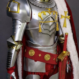 May include: A suit of silver plate armor featuring gold accents, a red fabric belt with gold circular emblems, and a long red cape with a white faux fur trim. A gold cross is attached to the cape, and a red sword with gold details is at the side.