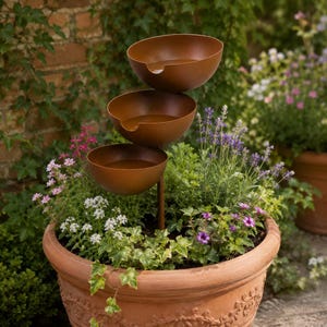 Farmhouse style garden water feature with rustic metal bowls installed among colorful backyard flowers.