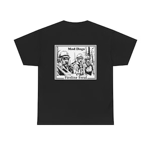 May include: A black t-shirt featuring a white graphic print on the back. The design shows three dogs wearing hard hats and safety gear in a forest setting, with the text Mod Dogs and Fireline Feral printed above and below the illustration.