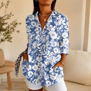 May include: A long-sleeved button-down shirt featuring a blue and white floral pattern. The shirt has a collar, a front button placket, and two side pockets. The fabric displays a repeating print of various flowers and leaves throughout the garment.