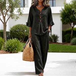 May include: A dark charcoal grey two-piece set consisting of a V-neck blouse with three large brown buttons and ruffled three-quarter length sleeves, paired with matching wide-leg trousers featuring side pockets and a relaxed, loose-fitting silhouette.