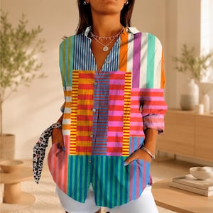 Puede incluir: Una camisa de manga larga con botones que presenta un vibrante diseño de patchwork con rayas verticales y horizontales en colores brillantes como naranja, rosa, azul, amarillo y blanco. La camisa tiene un cuello clásico y dos bolsillos.