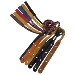May include: A collection of braided leather guitar straps in various colors including black, brown, tan, red, and blue. Each strap features a flat end with pre-punched holes for attachment and a textured, braided section that loops into a central knot.