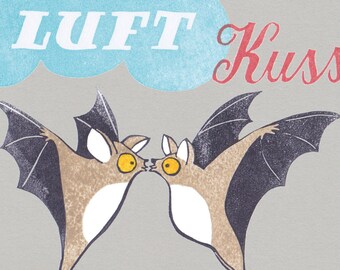 May include: Illustration of two cartoon bats kissing, with the words "LUFT Kuss" above them. The bats are brown with black wings and yellow eyes, set against a gray background.