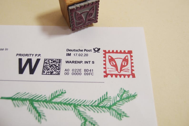 May include: A white envelope with a red and black stamp featuring a fox face. The envelope has a black barcode and the text "PRIORITY P.P. W" and "Deutsche Post IM 17.02.20 WARENP. INT S A0 022E BD41 00 0000 09FC".