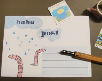 May include: A white postcard featuring the words "haha" and "post" in blue, with cartoon worms and raindrops. A pen and stamps are also visible.