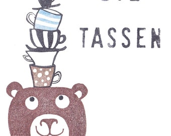 May include: A brown bear with big eyes and a smile is wearing a stack of five teacups on its head. The cups are decorated with stripes, polka dots, and black and white patterns. The text "Die Tassen" is printed above the bear.