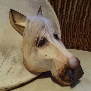 Könnte beinhalten: Handgefertigte Holzpferdskopfskulptur mit hellbraunem Finish und einer Mähne aus weißem Kunsthaar. Die Skulptur hat ein geometrisches Design und steht vor einem neutralen Hintergrund.