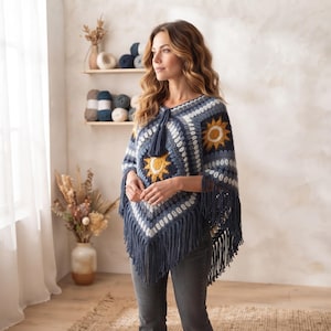 May include: A navy blue crochet poncho featuring a repeating sun motif in yellow and white. The garment is constructed from square panels with a textured stitch pattern and is finished with long, dark blue fringe along the bottom hem.