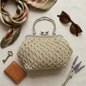 Könnte beinhalten: Eine beige gehäkelte Handtasche mit silbernem Metallrahmen und Griff, begleitet von einem gemusterten Schal, einer braunen Schildpatt-Sonnenbrille, einer kleinen braunen Ledergeldbörse, einem Metallschlüssel, einem goldenen Ring und getrocknetem Lavendel.