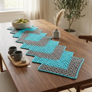 May include: A rectangular crochet table runner featuring a geometric pattern of alternating gray and bright turquoise yarn squares. The runner is composed of interconnected granny square motifs arranged in a zigzag design, creating a textured surface.