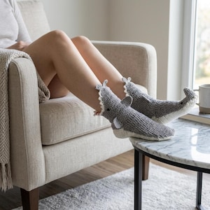 Peut inclure: Une paire de chaussettes en crochet gris et blanc en forme de requins. Les chaussettes présentent un corps supérieur gris, un ventre blanc, de petites nageoires latérales, une nageoire dorsale et une queue au talon. La gueule est ouverte.