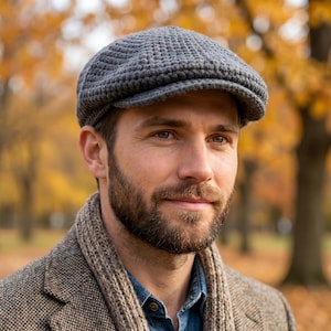May include: A grey crocheted flat cap featuring a textured, woven stitch pattern. The cap has a rounded crown and a short, stiffened brim extending from the front, constructed from a solid grey yarn with a consistent, dense knit texture.