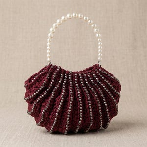 May include: A deep burgundy crochet handbag featuring a semi-circular pleated design with vertical rows of small dark metallic beads. The bag includes a single arched handle constructed from a continuous string of white spherical faux pearls.