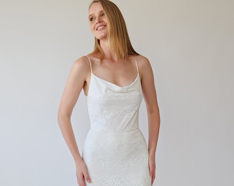 May include: A white lace mermaid wedding dress with a cowl neckline and spaghetti straps.