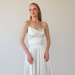 May include: A white satin dress with a cowl neck and a fitted bodice. The skirt is full and flowing, and the dress has a simple, elegant design.