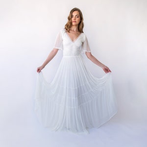 May include: A white wedding dress with a lace bodice and a flowing tulle skirt. The dress has short sleeves and a V-neckline.