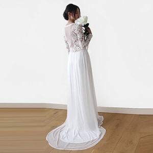 Puede incluir: Un vestido de novia blanco de encaje de manga larga con una falda de gasa fluida. El vestido tiene un panel trasero transparente y un escote redondo.