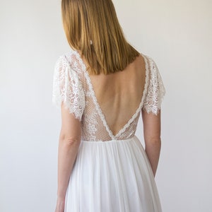 May include: A white lace wedding dress with a deep V-back and short sleeves. The dress is made of a lightweight fabric and has a flowing skirt.