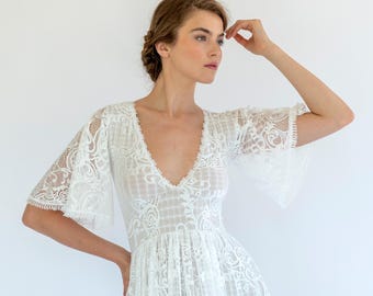 May include: A white lace dress with a plunging V-neckline and flared sleeves. The dress features intricate floral lace patterns and a delicate, flowing silhouette, perfect for a special occasion.