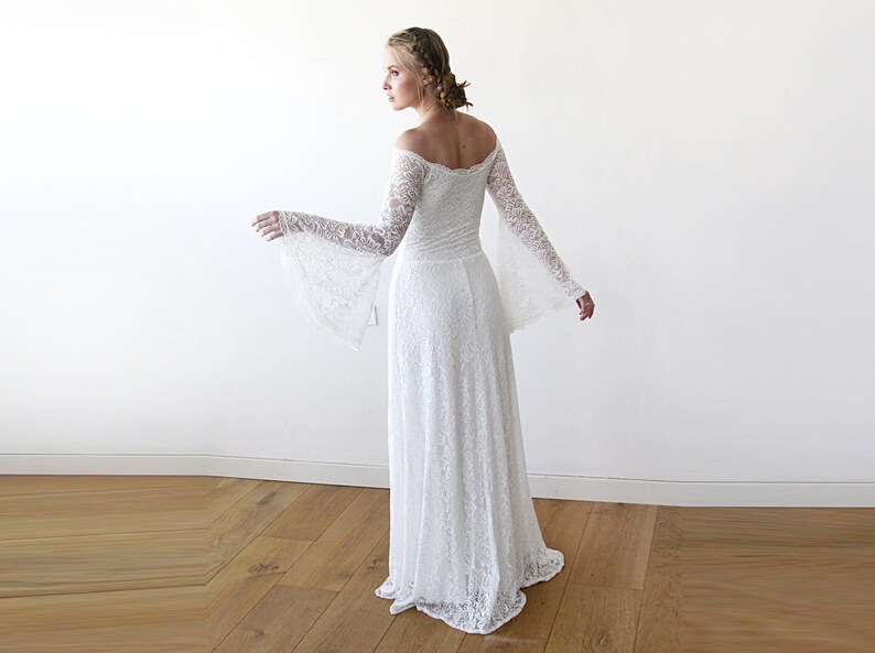 May include: A white off-the-shoulder lace wedding dress with long bell sleeves. The dress has a fitted bodice and a flowing skirt.