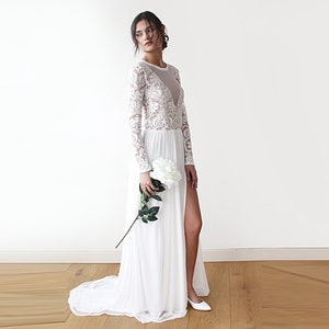 Puede incluir: Un vestido de novia blanco de encaje de manga larga con un corpi&ntilde;o transparente y una abertura alta en la falda.
