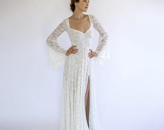 May include: A white lace wedding dress with long sleeves and a high neckline. The dress has a fitted bodice and a flowing skirt with a thigh-high slit.