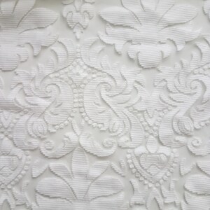 Puede incluir: Tela blanca con un patr&oacute;n floral en relieve. La tela tiene una textura delicada y de encaje.