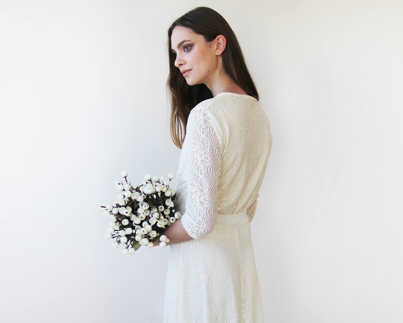 May include: A white lace wedding dress with a long sleeve and a fitted bodice. The dress has a flowing skirt and is paired with a bouquet of white berries.
