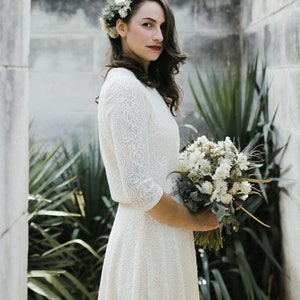 May include: A bride wearing a white lace dress with a floral crown and holding a bouquet of white flowers.
