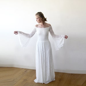 May include: A white off-the-shoulder lace wedding dress with long bell sleeves. The dress has a fitted bodice and a flowing skirt.