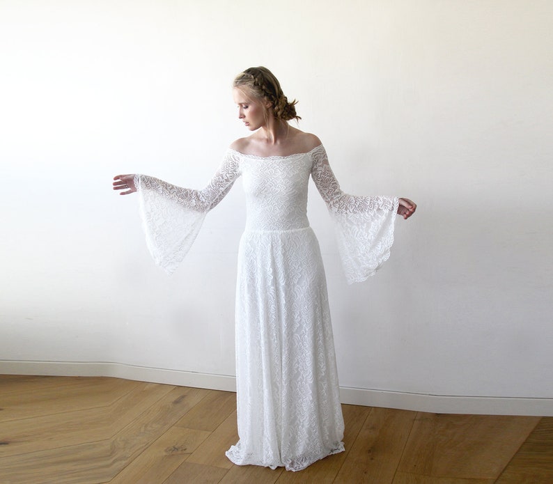 May include: A white off-the-shoulder lace wedding dress with long bell sleeves. The dress has a fitted bodice and a flowing skirt.