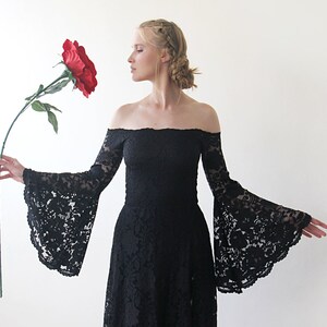 May include: A woman wearing a black off-the-shoulder lace dress with long bell sleeves, holding a large red rose.