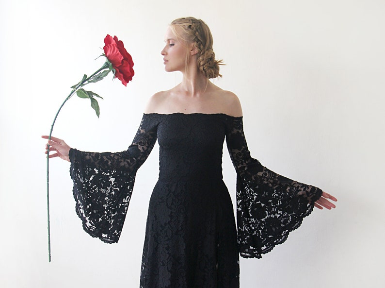 May include: A woman wearing a black off-the-shoulder lace dress with long bell sleeves, holding a large red rose.