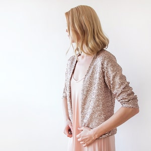 Puede incluir: Una chaqueta de lentejuelas de color oro rosa con mangas largas. La chaqueta es corta y tiene cuello en V.