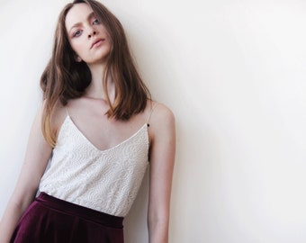 May include: A woman wearing a white lace top with a burgundy velvet skirt.