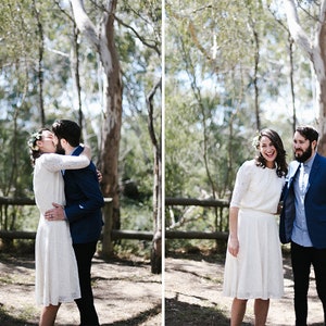 May include: A couple in a forest setting, the bride is wearing a white lace dress and a floral crown, the groom is wearing a blue suit jacket and a light blue shirt. The couple is kissing and smiling.